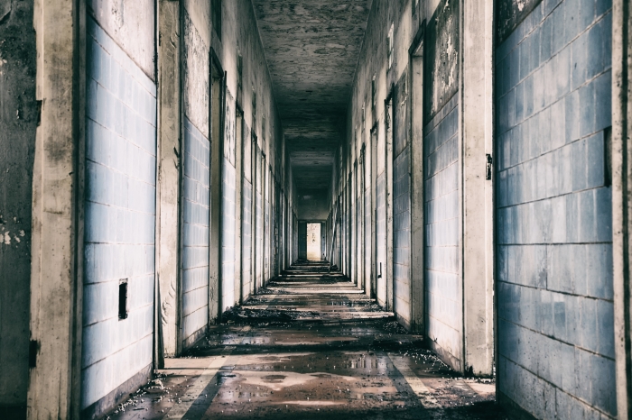 Long grey hallway of a dilapidated old asylum.